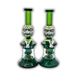 Decorative glass water pipe featuring carved tribal face artwork, frosted etched patterns, emerald green neck tubing, and detailed geometric base accents.