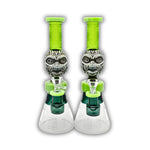 Frosted glass beaker bong with tribal mask centerpiece, neon green neck, geometric etched base, and matching green bowl accents.