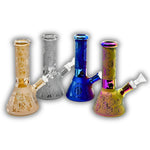 Assorted mini glass beaker bongs featuring frosted finishes, metallic electroplated colors, engraved paisley and skull patterns, cannabis leaf graphics, and decorative etched designs.