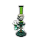 Decorative glass water pipe featuring carved tribal face artwork, frosted etched patterns, emerald green neck tubing, and detailed geometric base accents.