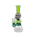 Frosted glass beaker bong with tribal mask centerpiece, neon green neck, geometric etched base, and matching green bowl accents.