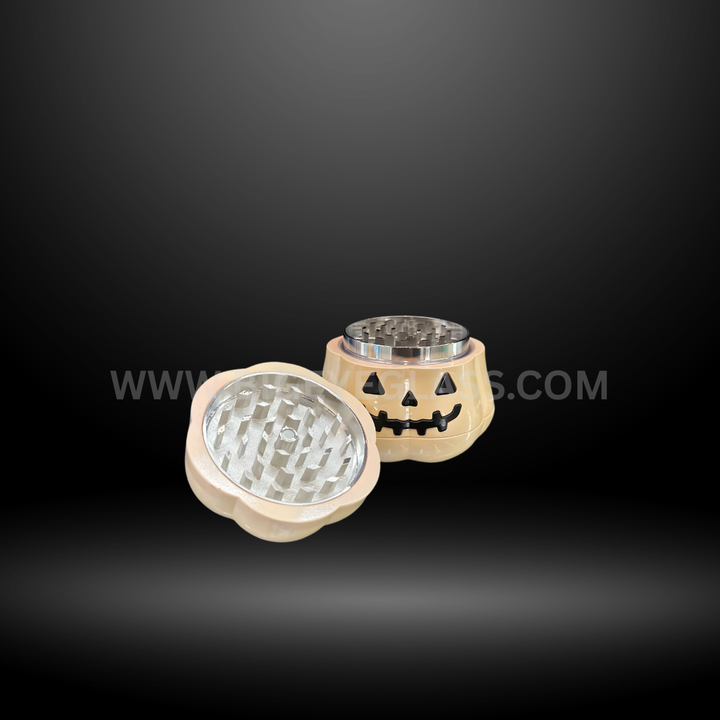 Pumpkin-shaped metal herb grinders in green, gold, and cream colors with smiling jack-o-lantern faces, displayed in Halloween packaging box.