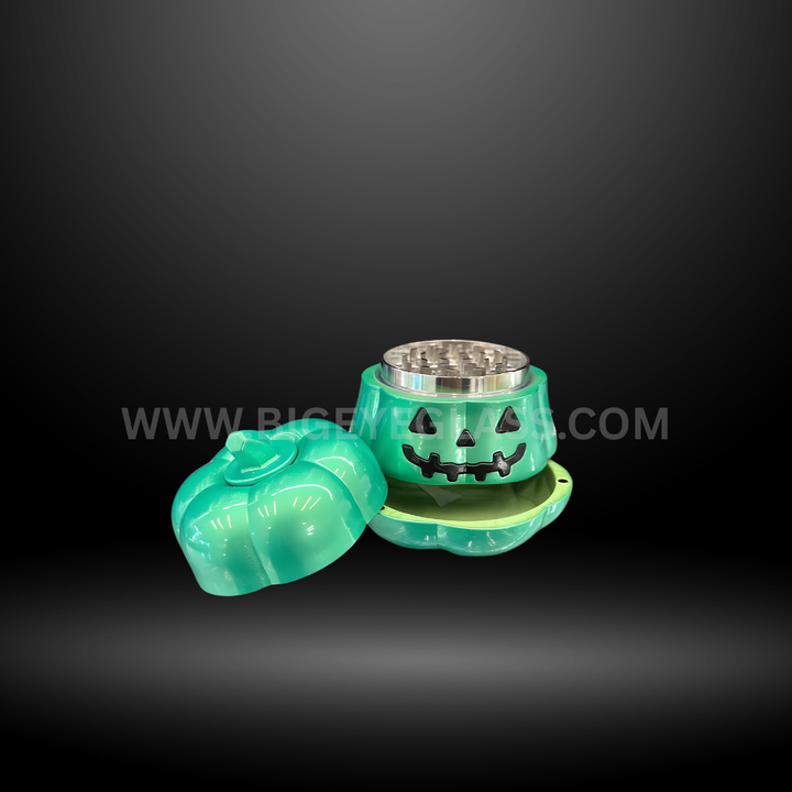 Pumpkin-shaped metal herb grinders in green, gold, and cream colors with smiling jack-o-lantern faces, displayed in Halloween packaging box.