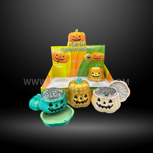 Pumpkin-shaped metal herb grinders in green, gold, and cream colors with smiling jack-o-lantern faces, displayed in Halloween packaging box.