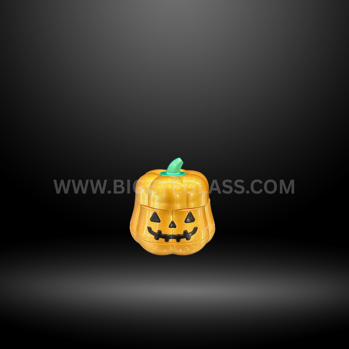 Pumpkin-shaped metal herb grinders in green, gold, and cream colors with smiling jack-o-lantern faces, displayed in Halloween packaging box.